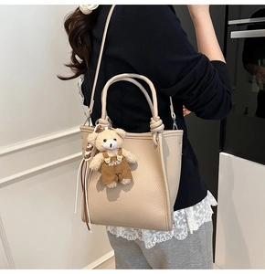 Close-up of beige lychee texture bucket bag with a cute teddy bear charm on shoulder