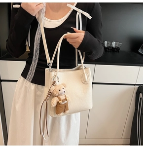 Detail of a creamy white lychee textured bucket bag with a cute bear plush charm attached