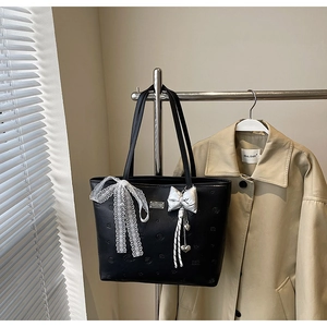 Detail of black leather tote bag featuring lace bow and silver heart pendant charm