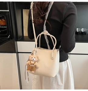 Close-up of creamy white lychee leather bucket bag featuring a cute plush bear pendant