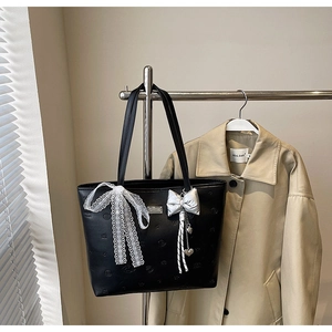 Detail of black embossed leather tote with lace bow and silver heart charms on a hanger