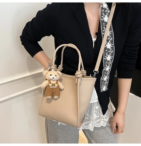 Détail du sac bandoulière beige avec pendentif ours et texture grainée élégante