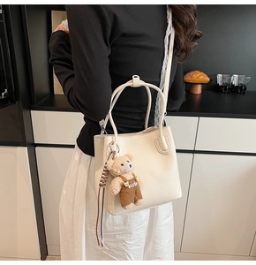 Detail of minimalist cream bucket bag featuring grainy texture and a cute bear charm