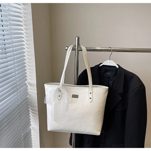 Close-up of white leather tote bag with embossed Saturn pattern and lace bow detail