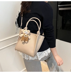 Detail of beige lychee leather tote bag featuring braided knot handles and a cute bear charm