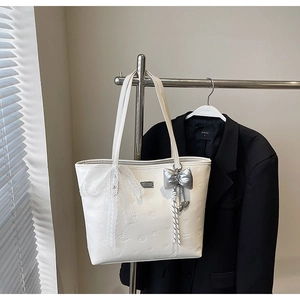 Close-up of white tote bag featuring embossed heart patterns and lace bow charm