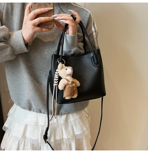 Close-up of black lychee grain leather bucket bag with cute plush bear charm on model