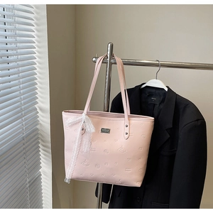 Detail of pink tote bag with embossed patterns and decorative lace bow on a dark blazer