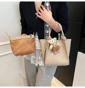 Detail of beige litchi leather bucket bag with knotted handle and cute bear charm