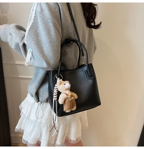 Detail of black lychee grain bucket bag featuring a cute plush bear charm on the side