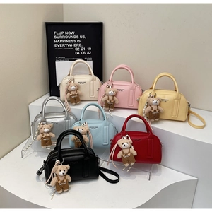 Detailed view of luxury boston bags in multiple colors with bear pendants on white podiums