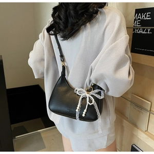 Détail du sac hobo en cuir grainé noir avec nœud en dentelle blanche et pendentif perle