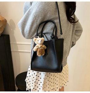 Detail view of black lychee grain tote bag with bear charm and adjustable shoulder strap