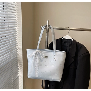 Macro detail of embossed faux leather tote bag with white lace ribbon and metal logo charm
