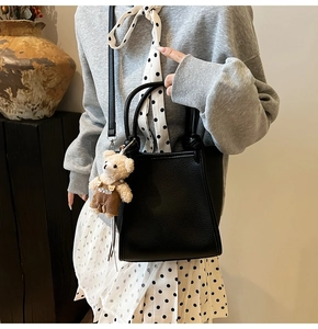 Detail of black pebbled leather crossbody tote bag with a cute plush bear charm on model