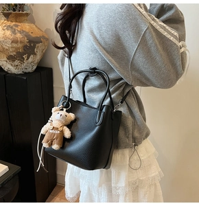 Detail of black lychee texture bucket bag with cute bear charm and adjustable strap