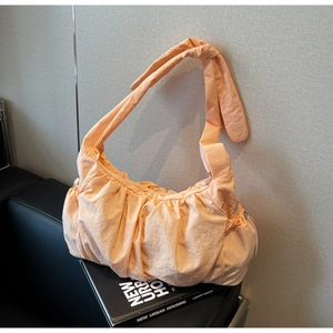 Detail of peach pleated nylon crescent bag with knotted shoulder strap on leather sofa