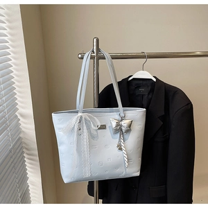 Detail of light blue tote bag with heart embossing and white lace bow accessory