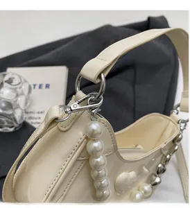 Detail van crème lakslederen handtas met parelketting en metalen hartvormige bedels