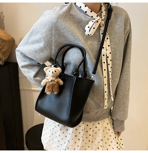 Détail du sac seau en cuir grainé noir avec un adorable pendentif ours en peluche