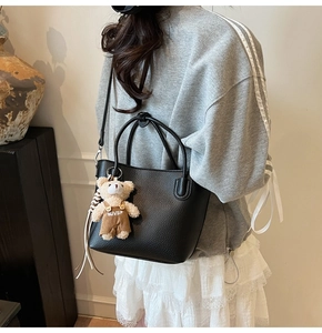 Close-up of black lychee grain bucket bag with cute bear charm and shoulder strap
