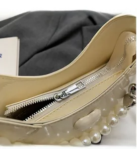 Detailopname van de gladde metalen rits en decoratieve parels op een beige handtas