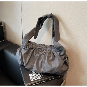 Detail of dark grey pleated nylon hobo bag with knotted shoulder strap on a chair