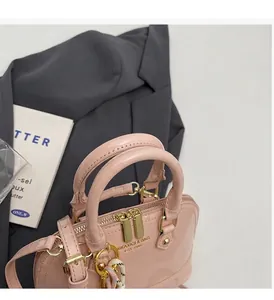 Detail of pink patent leather shell bag featuring golden logo and sturdy handles