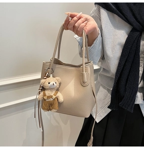 Detail of beige bucket bag featuring pebbled leather texture and cute plush bear charm