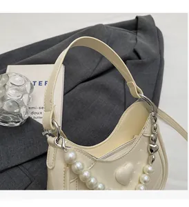 Detail van crème hobo tas met hartjesreliëf, parelketting en hartvormige metalen bedeltjes