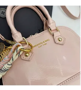 Close-up of pink patent leather handbag featuring gold branding and decorative tennis pendant