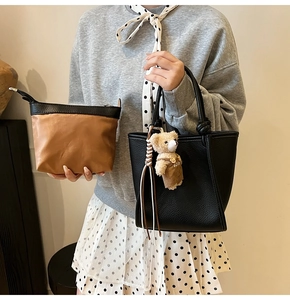 Detail of black pebbled tote bag with plush bear charm and brown zippered pouch