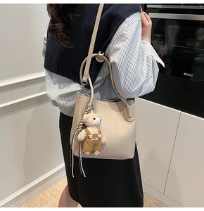 Beige pebble texture bucket bag with cute bear charm and adjustable shoulder strap worn by model