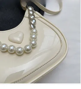 Detail van een crèmekleurige lakschoudertas met parelketting en hartvormig beslag