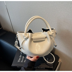 Detail der glänzenden cremeweißen Beuteltasche mit Knotengriff und Kordelzug-Metallkugeln