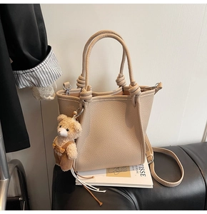Detail of beige lychee grain tote bag with rope knot handles and teddy bear charm