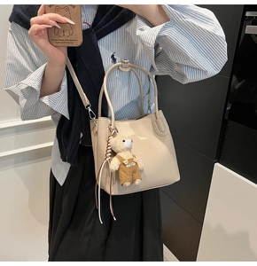 Detail of off-white lychee leather bucket bag with silver hardware and a cute teddy bear charm