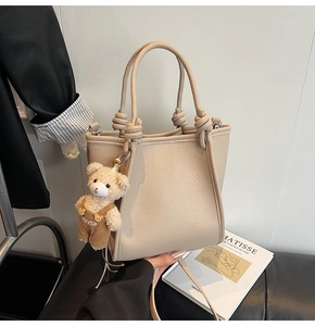 Detailed texture of beige lychee grain leather handbag with a cute bear charm pendant