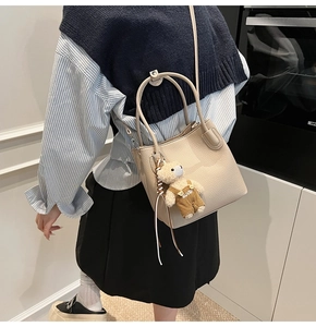 Detail of beige litchi grain leather bucket bag with a cute plush bear pendant accessory