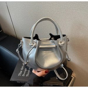Makro-Detail der silbernen Metallic-Eimertasche mit Knotengriff auf einem Buch
