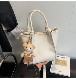 Detail of white lychee leather bucket bag with woven handles and brown bear charm