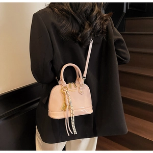 Detail of pink patent leather shell bag worn as a crossbody with metal logo