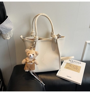 Detail of off-white lychee leather bucket bag with knot handle and teddy bear charm