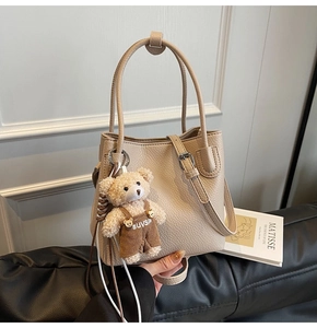 Detail of apricot bucket bag in pebble leather with a cute bear charm on a sofa