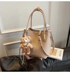Close-up of beige lychee grain bucket bag featuring a cute teddy bear pendant detail