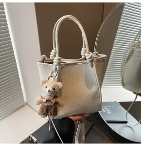 Detailed shot of a white lychee grain bucket bag featuring a knot handle and bear pendant