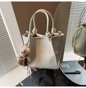 Detail of white lychee leather bucket bag with a cute teddy bear charm and knotted handles