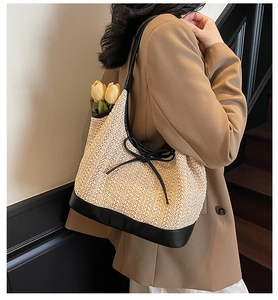 Detail of woven straw tote bag featuring black piping, long straps and bow decoration