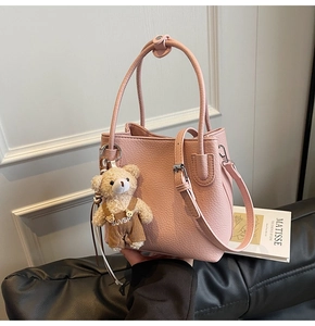 Detail of light pink pebble leather bucket bag featuring a plush bear charm and dual handles