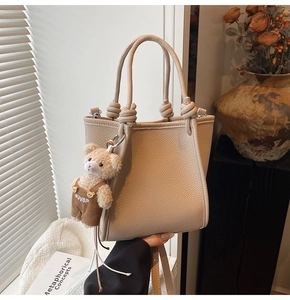Detail of beige lychee textured bucket bag with decorative knot handles and plush bear charm